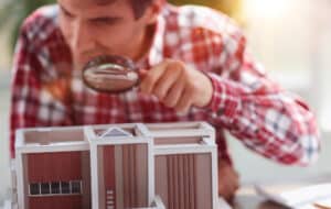 male appraiser looking at house model through magnifying glass.